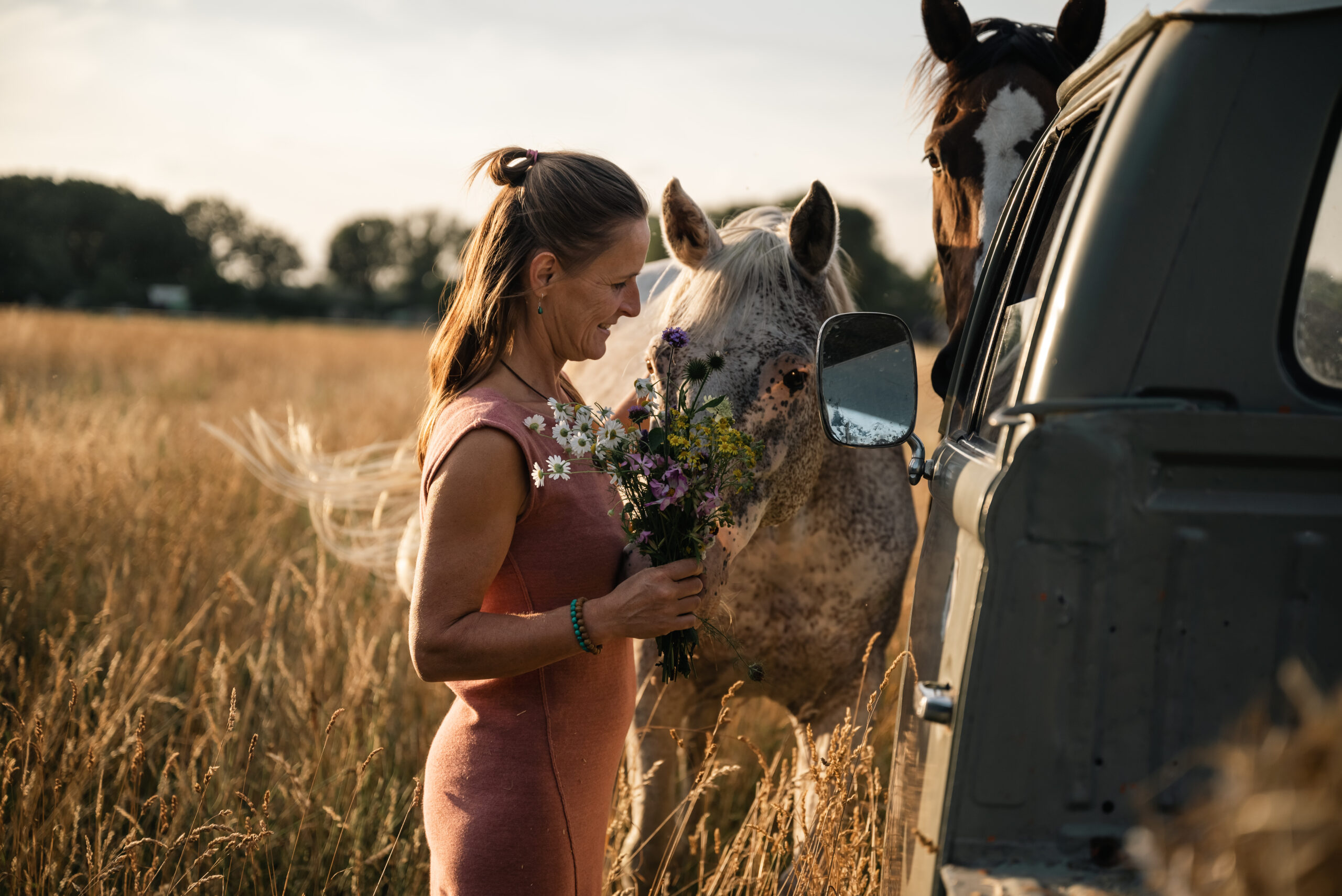 Vrouw in verbinding met paarden en bloemen tijdens bezielde fotosessie in het veld, begeleid door energetisch therapeut Daisy Kirkels